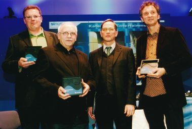 Das Bild zeigt vier Männer bei einer Preisverleihung im Rahmen der Prolight + Sound. Drei von ihnen halten Auszeichnungen in der Hand, auf denen „Sinus“ steht: Sie gewannen den Sinus - Systems Integration Award. Die Männer tragen überwiegend formelle Kleidung, von Anzügen bis zu eleganten Sakkos. Im Hintergrund ist eine blaue Wand mit dem Schriftzug „Sinus“ und weiteren Informationen sichtbar, die die Veranstaltung professionell einrahmt. Die Gesichter der Ausgezeichneten strahlen Stolz und Freude aus, was die Bedeutung des Moments unterstreicht.