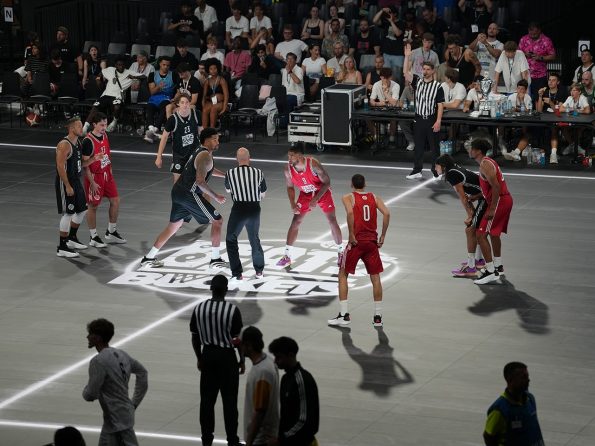 Basketball game on a modern glass floor at an event – jump ball scene in front of a full crowd.