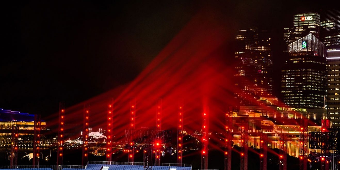 claypaky-hy-b-eye-k25-singapores-bicentennial-ndc
Das Bild zeigt eine nächtliche Szene mit einer beeindruckenden Lichtinstallation. Mehrere vertikal aufgereihte rote Lichtstrahlen ragen in den Himmel und erzeugen eine dynamische Atmosphäre. Im Hintergrund sind beleuchtete Hochhäuser zu sehen, darunter das Fullerton Hotel sowie Gebäude mit markanten Logos. Die Szenerie vermittelt den Eindruck einer groß angelegten Veranstaltung, möglicherweise in einer urbanen Umgebung wie Singapur. Die Lichtinstallation dürfte von leistungsstarken LED-Moving-Heads wie dem Claypaky HY B-EYE K25 stammen, die bekannt für ihre brillante Farbintensität und Vielseitigkeit sind.