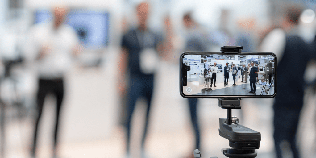 Smartphone auf Stativ filmt Event für Streaming mit Influencern in moderner Messehalle