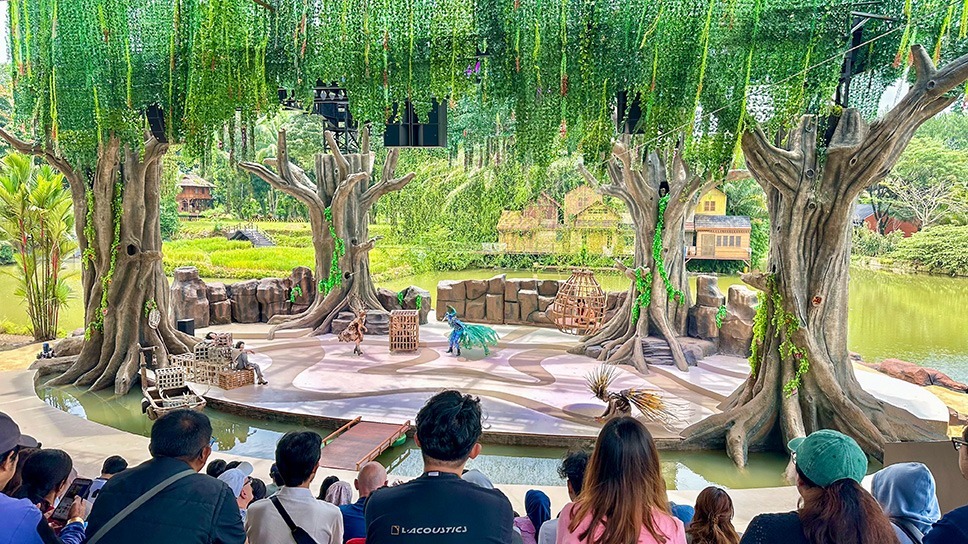 Open-air theatre with an audience and stage surrounded by tropical vegetation
