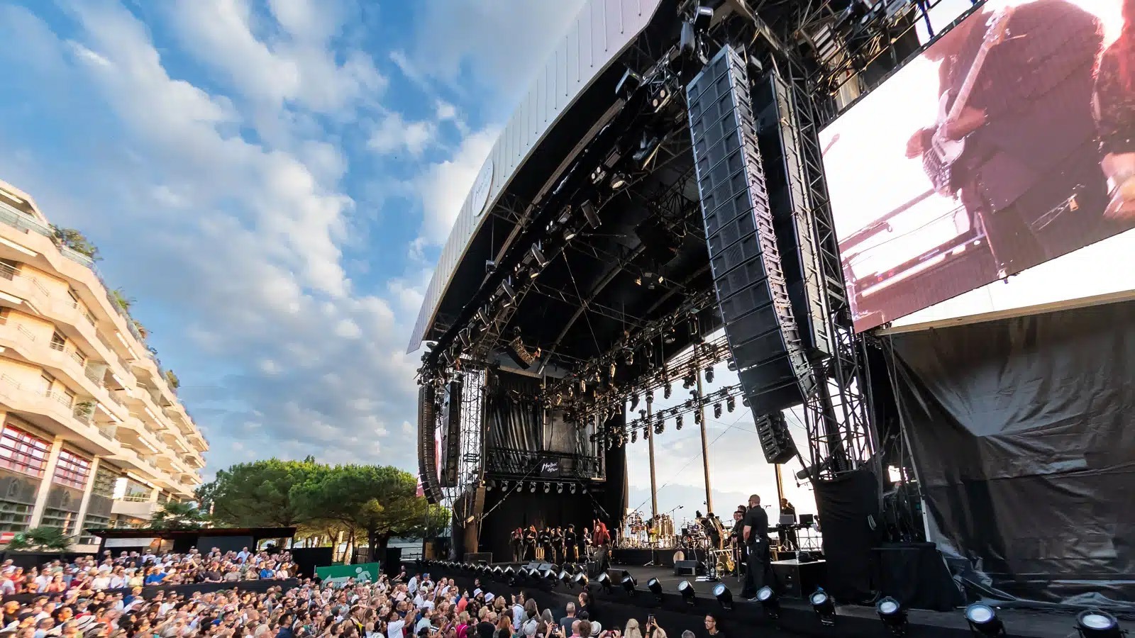 Open-air stage with large loudspeaker arrays and an audience in sunny weather