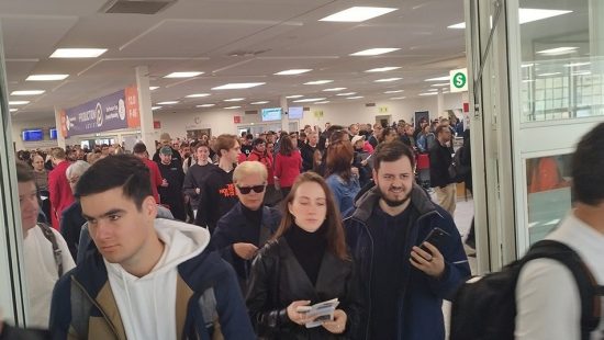 Auf dem Bild ist ein stark frequentierter Eingangsbereich einer Messe oder Veranstaltungshalle zu sehen – offenbar gerade zur Öffnung oder unmittelbar nach Beginn des Events. Hunderte Menschen strömen durch breite Türen in die Halle, viele mit Tickets, Smartphones oder Broschüren in der Hand. Die Stimmung wirkt geschäftig, aber geordnet.

Im Hintergrund erkennt man ein großes Banner mit dem Schriftzug "Production + DJ" sowie Hallennummern (z. B. 12.0, F 46), was auf einen Messekontext hindeutet – vermutlich die Prolight + Sound 2025. Auch die Wegweiser und Monitore zur Orientierung sowie die „S“-Schilder (vielleicht für „Service“ oder „Shuttle“) verstärken den Eindruck eines professionell organisierten Großevents.

Das Bild vermittelt den Moment des Ansturms: viele Besucher, teils in Gruppen, teils einzeln, die sich auf den Weg in die Ausstellungsbereiche machen. Es zeigt, wie groß das Interesse an der Veranstaltung ist.