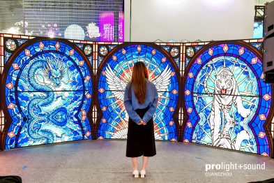 Besucherin betrachtet leuchtende Displaykunst mit Drachen- und Tigermotiv.