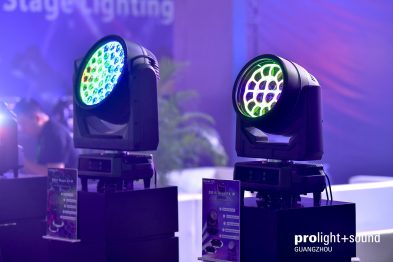 Zwei Moving Heads leuchten farbig vor violettem Messehintergrund