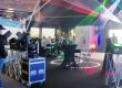 Messestand von Pluslite mit Scheinwerfern, Lichtstrahlen und Besuchergruppe in Gesprächen.