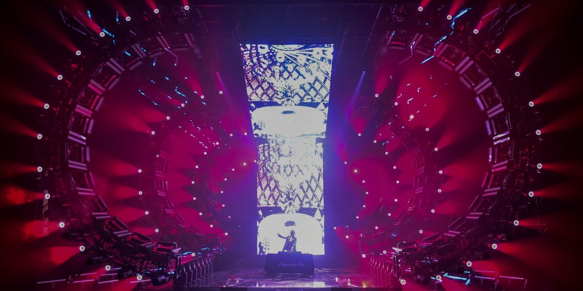 DJ in front of LED wall, surrounded by red moving lights and circular stage.