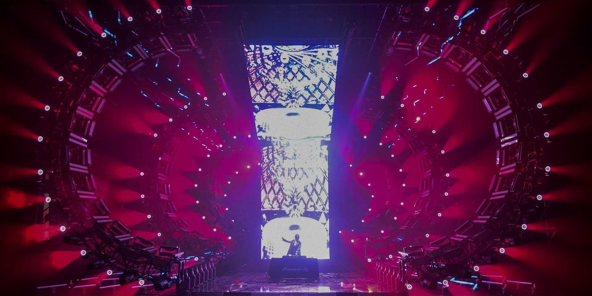 DJ in front of LED wall, surrounded by red moving lights and circular stage.