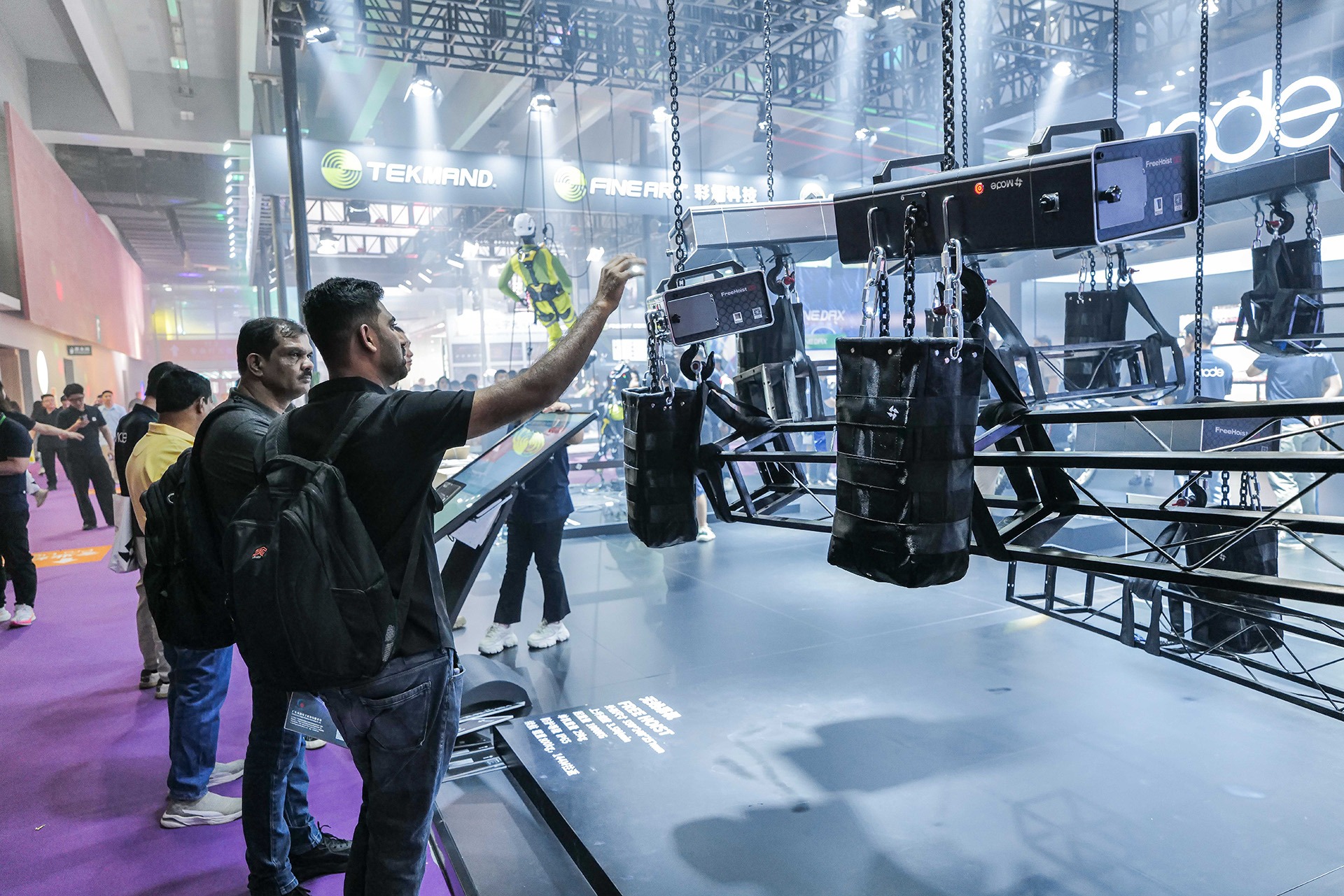 Visitors view a rigging setup with chain hoists and weights in an exhibition hall.
