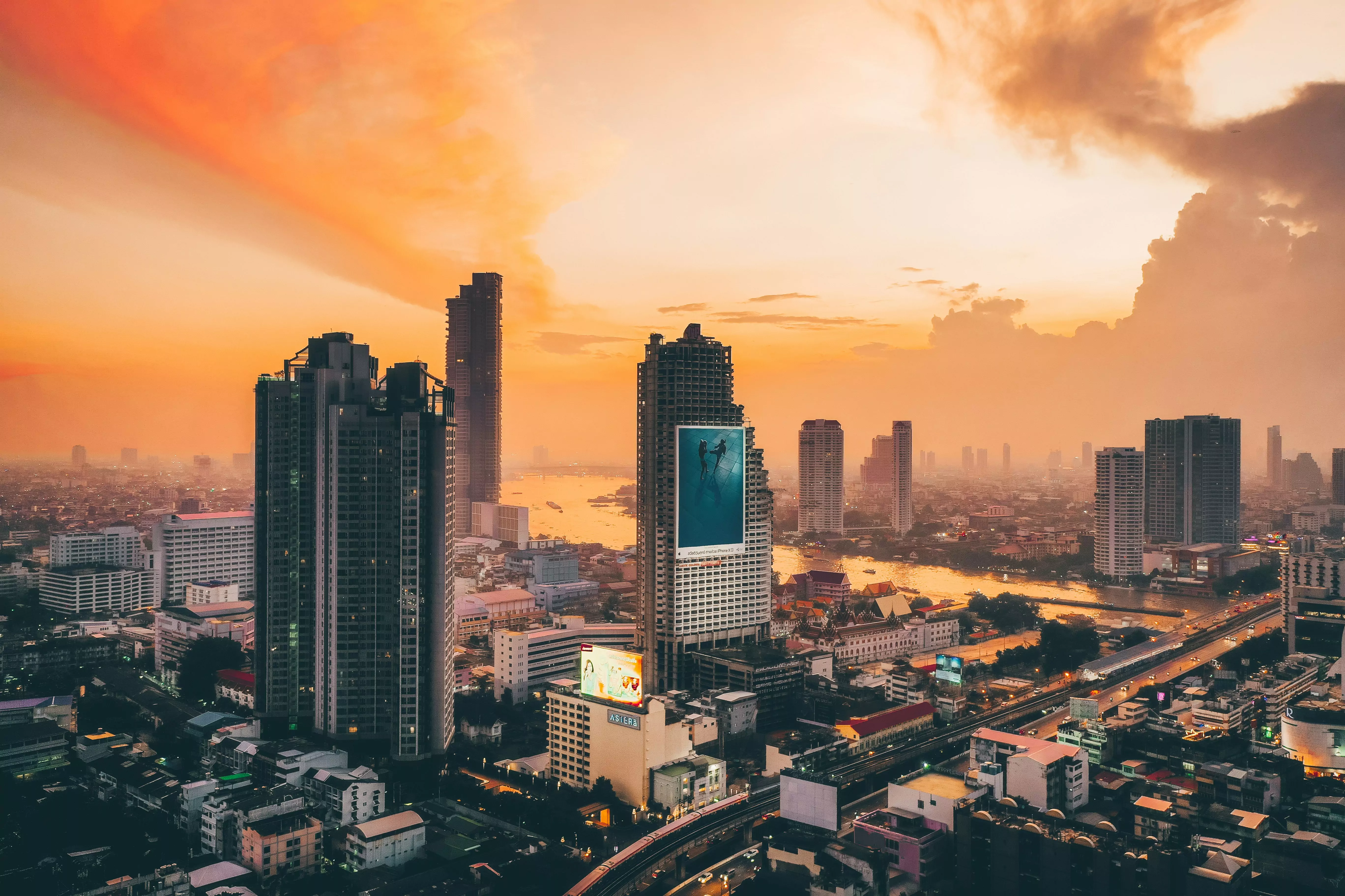 The Bangkok skyline along the river at sunset, featuring skyscrapers and streets.