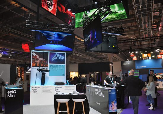 Messestand von Tait mit epiQ Mini Console, Bildschirmen und Besucherinnen und Besuchern auf Messe.