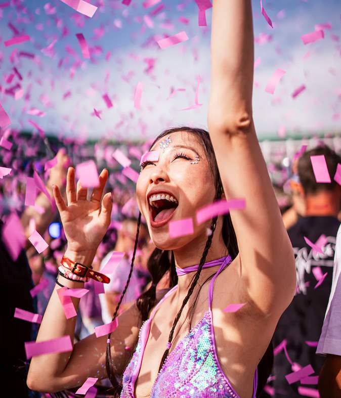Festivalgoer cheering with raised arm amid pink confetti
